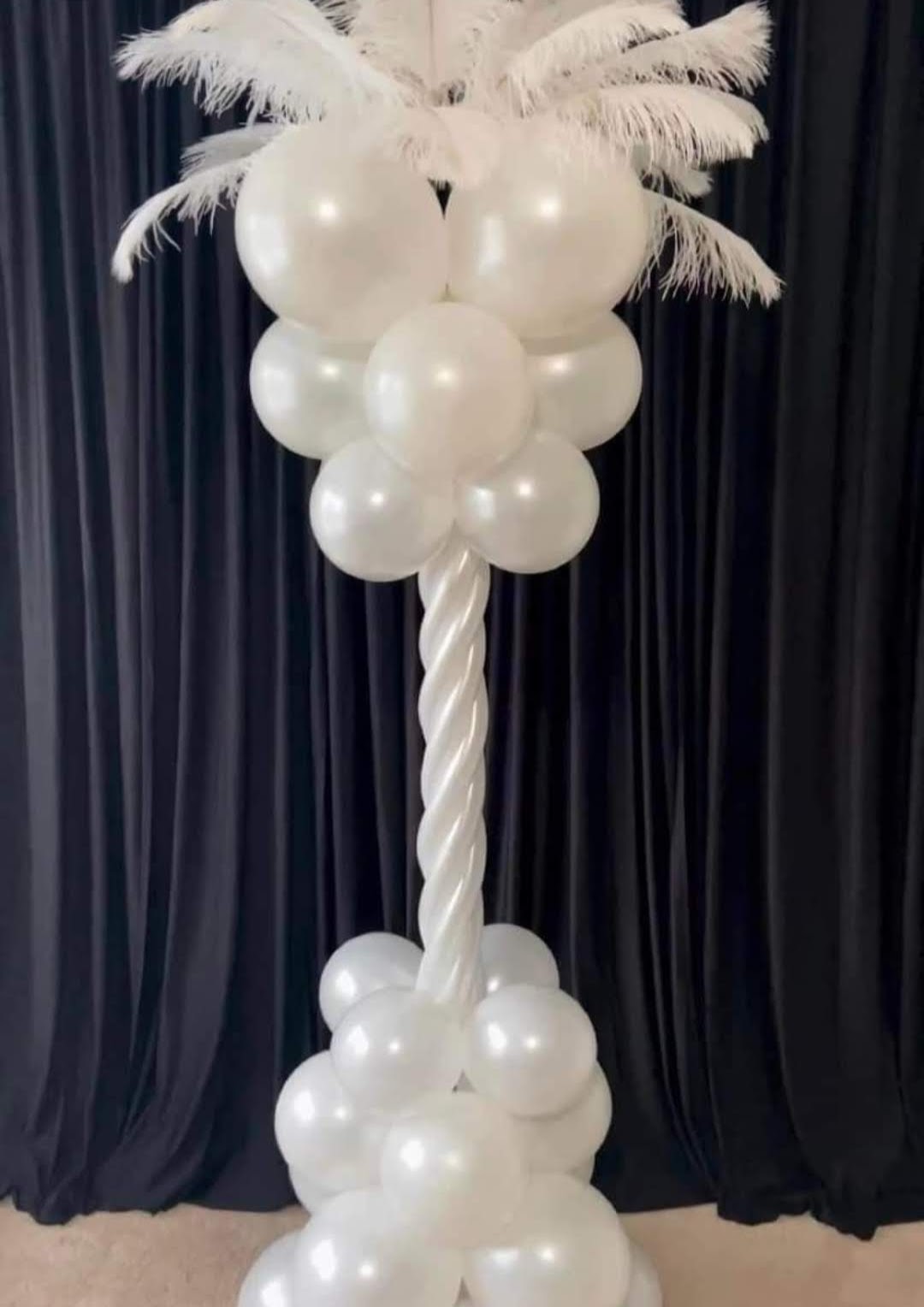 a tall white balloon column with feathers and balloons